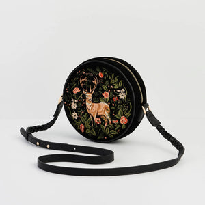 Angled side view of embroidered black round crossbody bag featuring woodland stag and floral design.