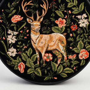 Close-up of intricate woodland stag and wildflower embroidery on black velvet circle bag.