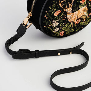 Detail shot of black adjustable faux leather strap and gold zip on embroidered velvet circle bag.