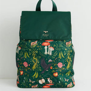 Front View: A green nylon backpack featuring Catherine Rowe’s Into the Woods fairytale print, with a fold-over flap, gold bee emblem, and intricate woodland illustrations.