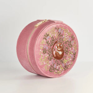 A round pink velvet jewellery box featuring an embroidered dormouse nestled among floral details. The box has a gold zip closure.