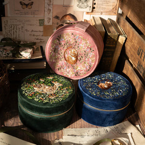 A collection of round velvet jewellery boxes in pink, green, and blue, each with embroidered woodland animal designs, placed among vintage-style décor.