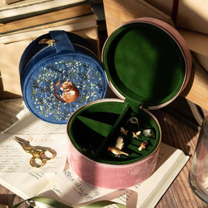 The pink and blue dormouse jewellery boxes displayed in a cosy setting, filled with jewellery pieces, placed on an open book with vintage stationery.