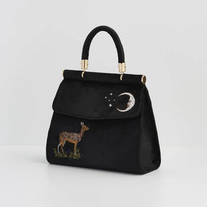 Side Angle: A three-quarter view of the black velvet tote, showcasing its structured form, gold-tone metal accents, and embroidered celestial moon and deer motif.