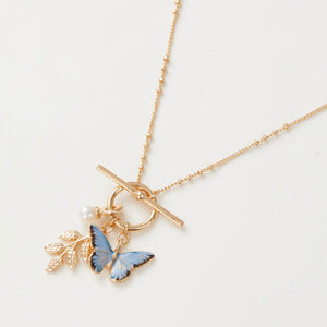 Close-up of gold necklace with blue enamel butterfly, leaf charm, and pearl on T-bar fastening.