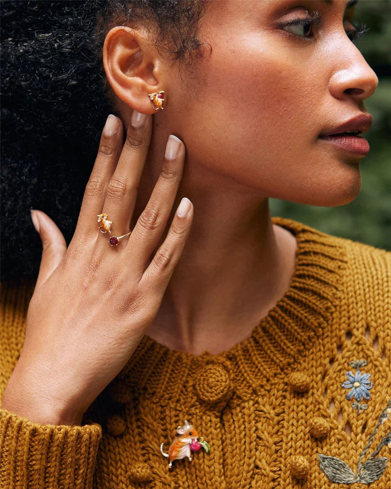 Lifestyle Image: A model wearing the Fable England Enamel Vole Brooch on a mustard knit sweater, along with matching vole earrings and a cherry-accented ring, showcasing the brooch’s whimsical woodland charm in a natural setting.