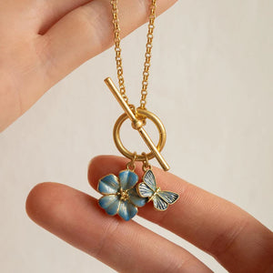 Hand holding the necklace, highlighting the delicate craftsmanship of the enamel-painted butterfly and flower charms.