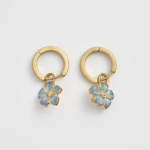 Front view of the Forget Me Not Charm Huggie Earrings – a pair of gold huggie hoops with blue enamel flower charms.