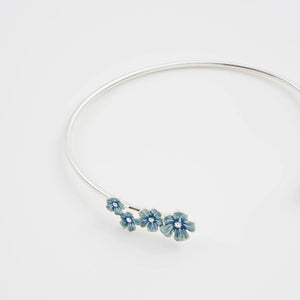 Close-up of silver bangle showing hand-painted forget-me-not flowers in blue enamel detail.