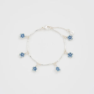 Dainty silver bracelet with blue forget-me-not charm displayed on white background.