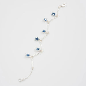 Close-up of enamel forget-me-not charm on silver chain bracelet.