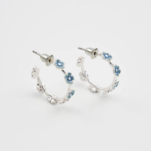 Front view of Fable Forget-Me-Not silver stud hoop earrings with hand-painted blue floral enamel on twig-textured hoops,