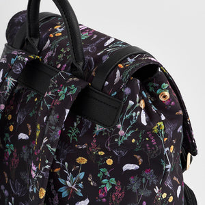 Close-up of snap-button flap closure and top carry handle on Fable England black backpack with wildflower print.