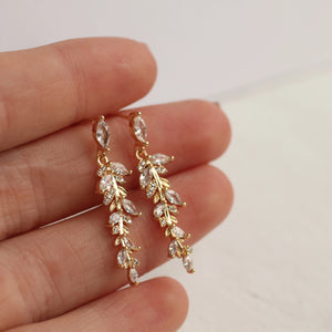 A close-up of a hand holding the delicate feather fern drop earrings, showcasing the intricate details and shimmering stones.