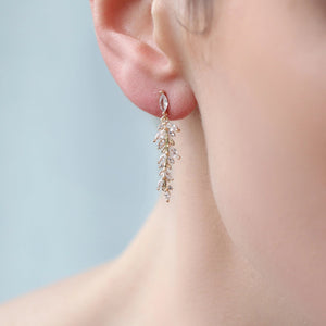 A single feather fern drop earring worn on an ear, highlighting its elegant length and sparkling design against a soft, blurred background.