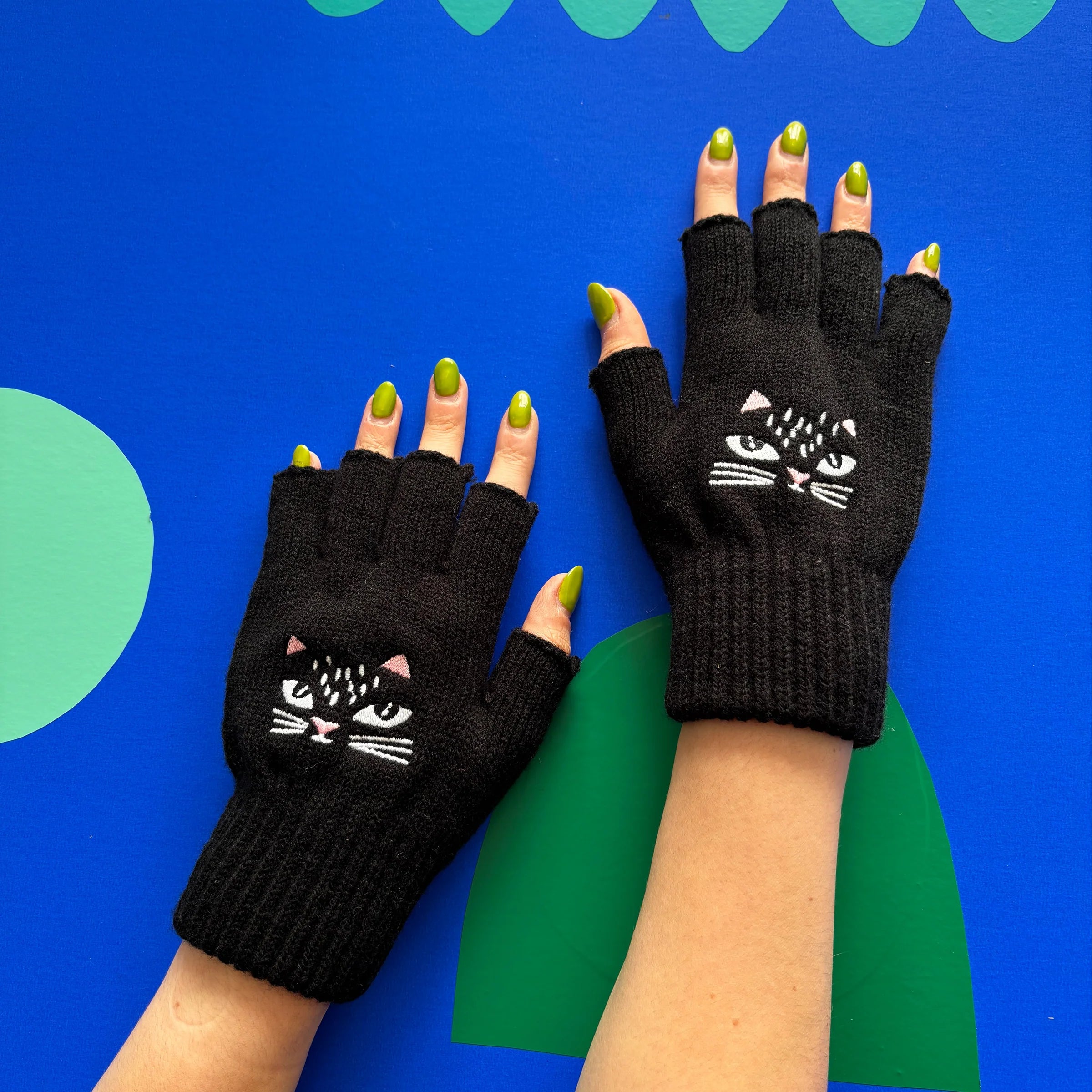 Feline Fingerless Gloves with embroidered cat face design worn on blue background.