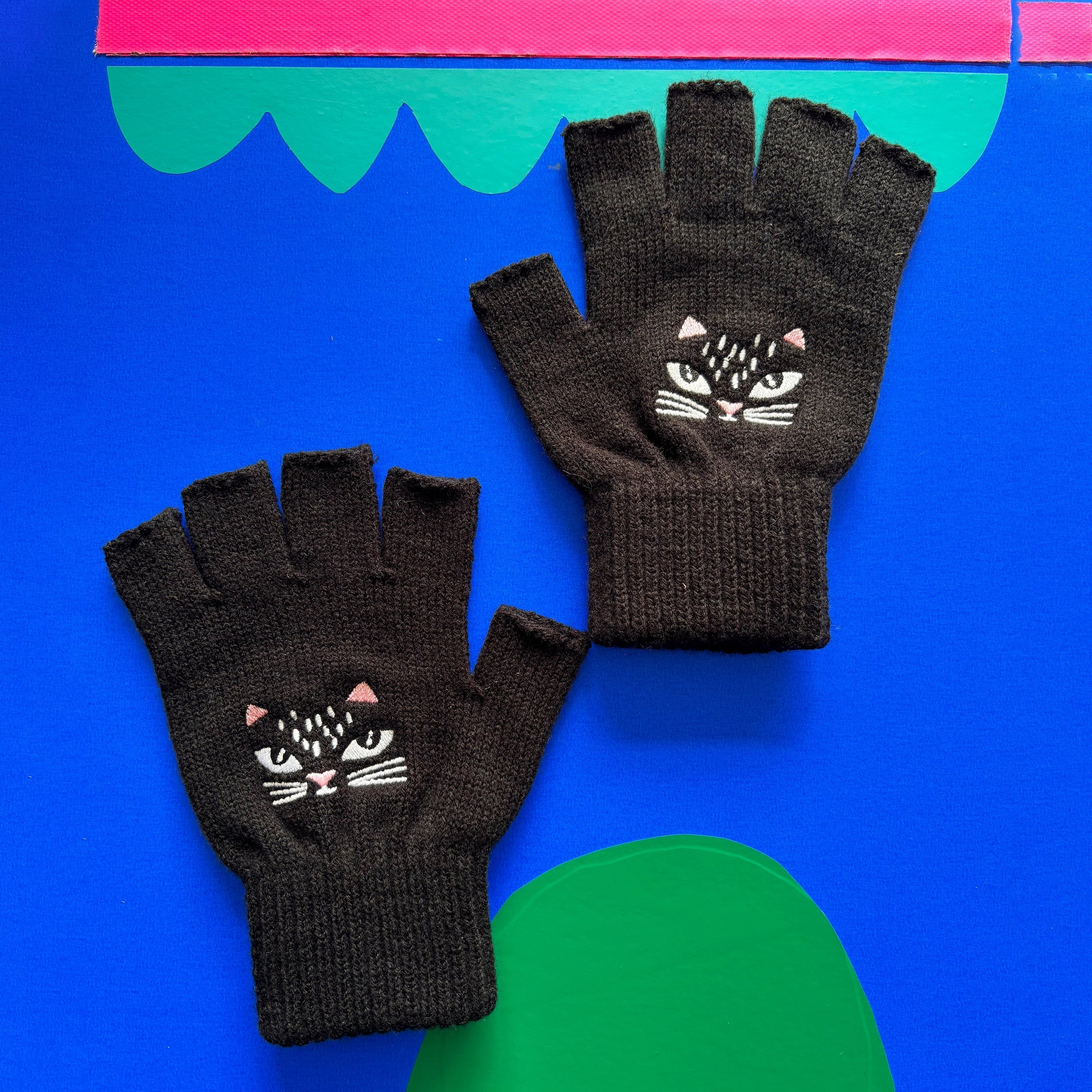 Flat lay of black knitted fingerless gloves with white whisker detail.