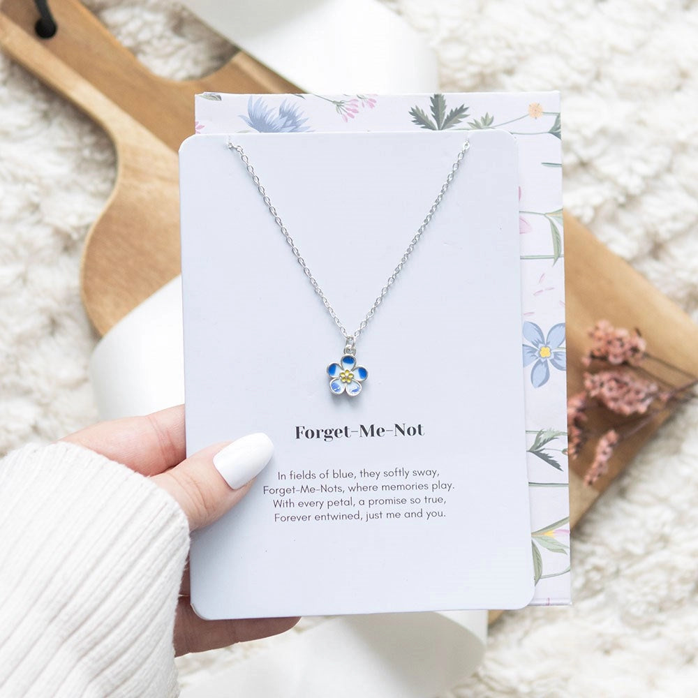 Hand holding a forget-me-not flower necklace presented on a floral greeting card, perfect for gifting.