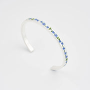 Sterling silver bangle with delicate forget-me-not flower charm on plain white background.