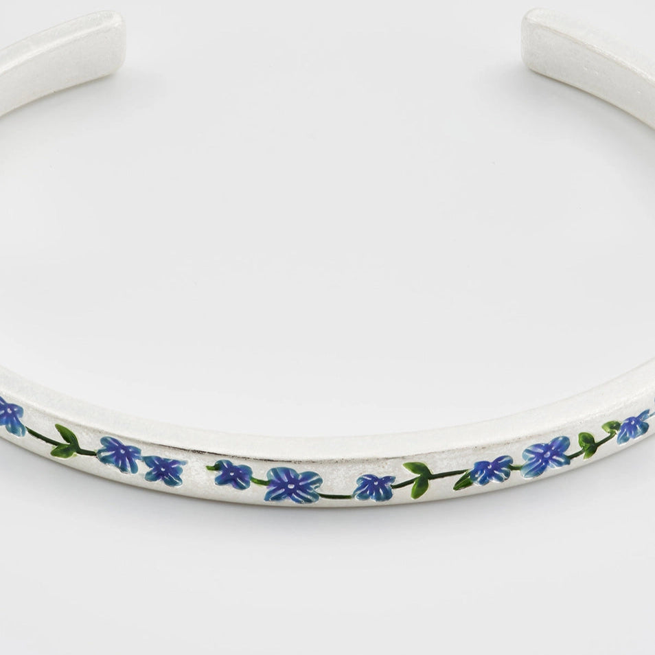 Flat lay of silver bangle with small blue enamel forget-me-not flower charm.