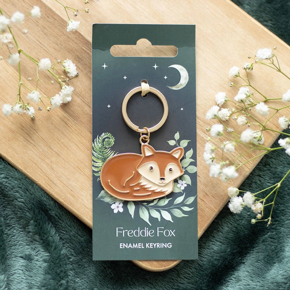 Freddie Fox enamel keyring displayed on illustrated forest-themed backing card with moon and foliage.