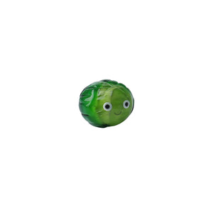 Angled view of quirky green glass Brussels sprout bauble on plain background.