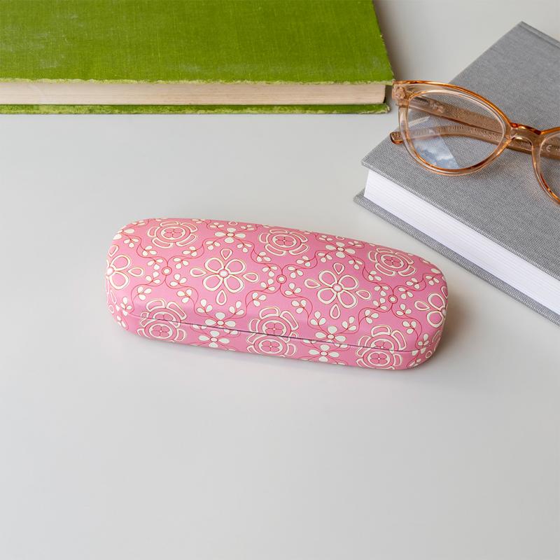Front view of Anushka pink floral glasses case on a desk beside books and glasses.