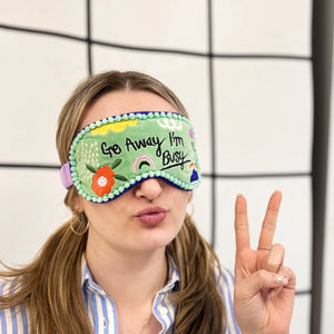 Model wearing Go Away I’m Busy green velvet eyemask with floral embroidery, peace sign raised.