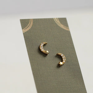 Close-up of gold vermeil moon and star stud earrings with crystal accents on a neutral background.