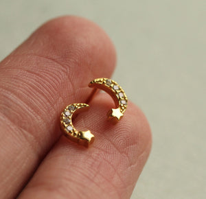 Gold crystal moon earrings held on fingertips showing petite size and detailed texture.