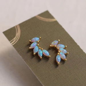 Gold vermeil opal wing stud earrings placed on a textured green linen presentation card, showcasing their elegant design and iridescent opals.