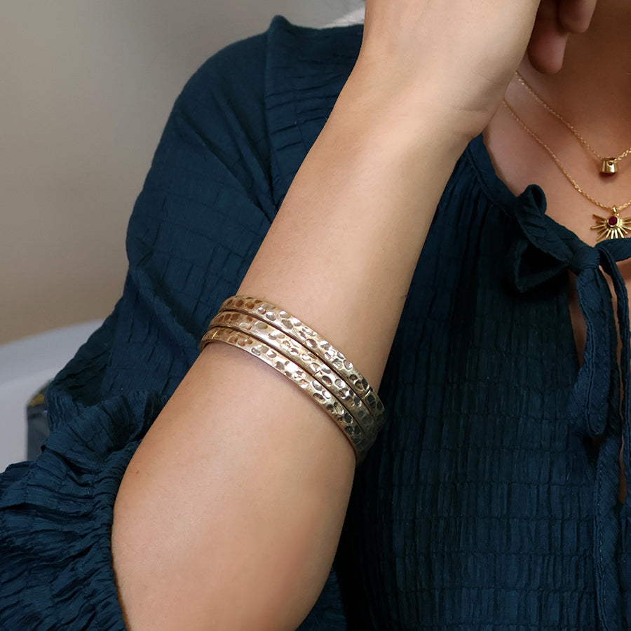 Woman wearing triple gold bangles styled with navy blouse and gold necklace.