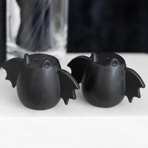 Gothic bat wing salt and pepper shakers on white table, matte black finish with pointed ears and spread wings.