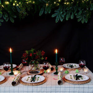 Festive Christmas dinner table with red wine, greenery, and glowing dark green glass candle holders topped with taper candles.