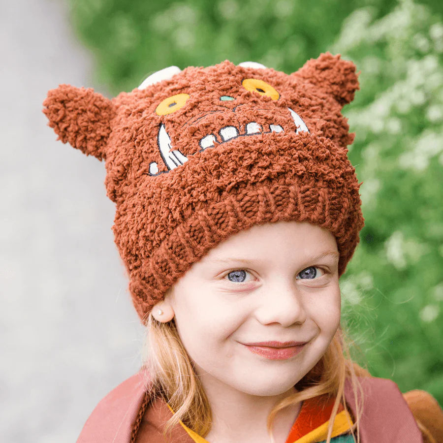Child wearing Gruffalo Winter Hat smiling outdoors, showing orange eyes and white horns.