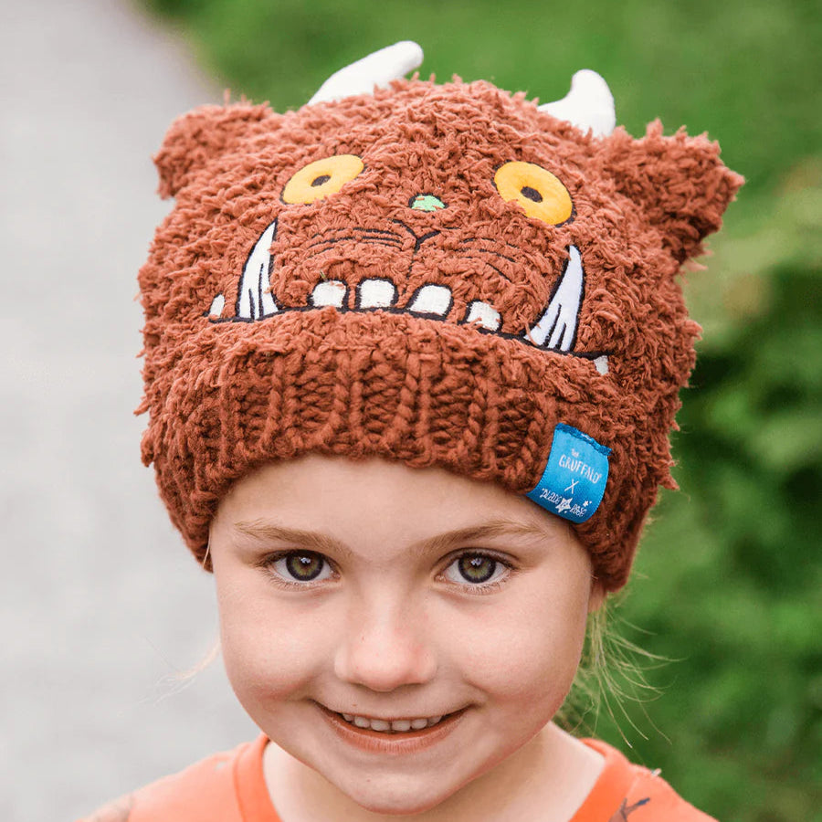Little girl wearing Gruffalo Winter Hat and orange Gruffalo top, smiling on a woodland path.