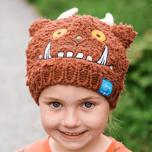 Little girl wearing Gruffalo Winter Hat and orange Gruffalo top, smiling on a woodland path.