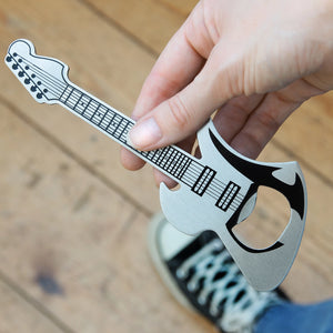 Hand holding a guitar-shaped bottle opener on a wooden surface