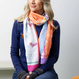 A woman with blonde hair wearing a Hairy Coo Highland Cow scarf in Coral, styled around her neck over a navy blue top.