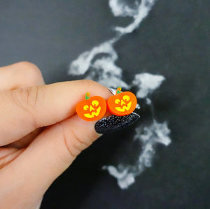 Front view of Halloween pumpkin stud earrings with glowing faces.