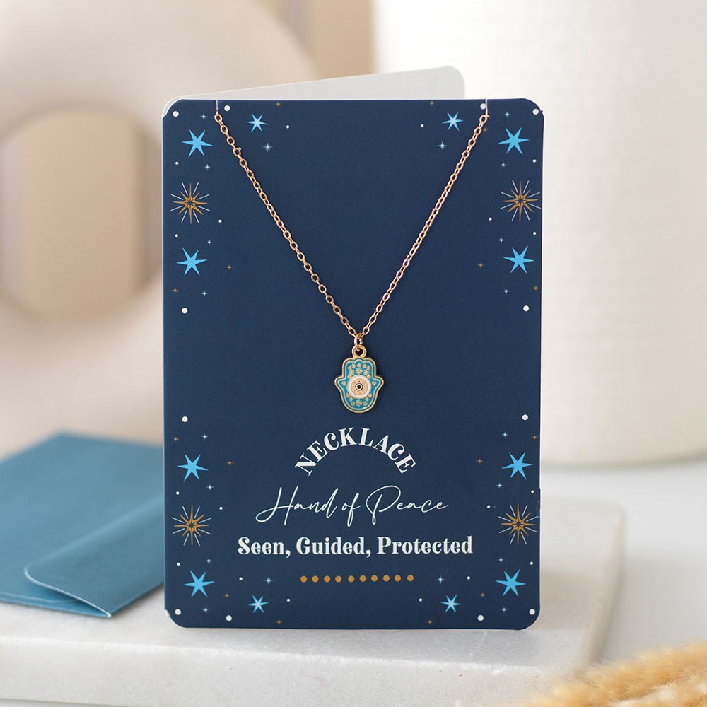 Hand of Hamsa necklace displayed on navy starry greeting card with envelope in background.