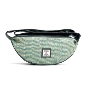 Front view: Harris Tweed Sling Bag in turquoise, highlighting the bag's dimensions, vegan leather trim and Harris Tweed Orb trademark badge.