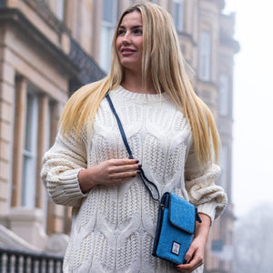 Woman wearing sky blue Harris Tweed mini crossbody bag with navy strap over white jumper in city street setting.