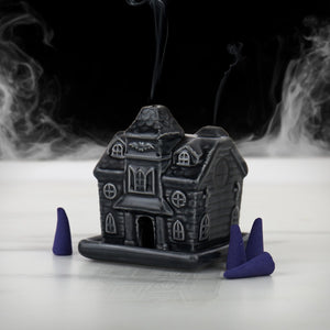 Dark ceramic haunted house incense burner emitting smoke with purple lavender incense cones surrounding it.