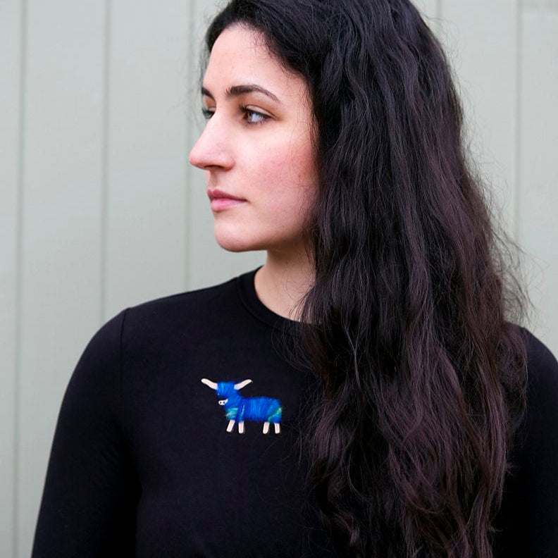 Blue and green tartan-inspired Highland coo brooch on a black top.