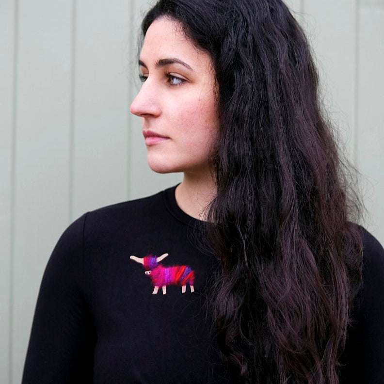Vibrant pink and purple Highland cow brooch on a black outfit.
