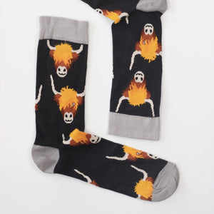 Flat lay of Highland Cows Men’s Bamboo Socks, showing detailed cow print design with grey cuffs, heels, and toes on a dark background.