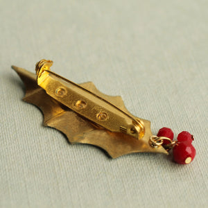 Gold-plated backing and secure brooch clasp on the reverse side of a holly leaf pin with dangling red berry beads.