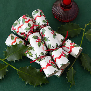Mini Christmas crackers styled on a green tablecloth with real holly leaves and red candle, showcasing festive holly print and red ribbon.