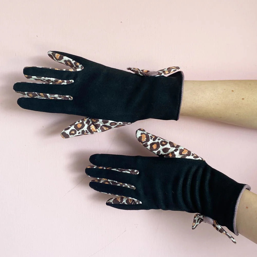 Pair of black gloves with leopard print trim displayed on arms against pink background.